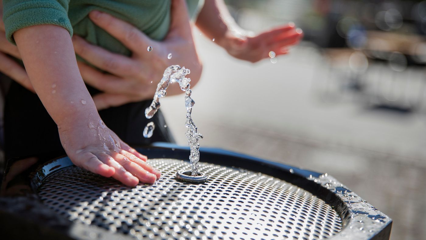 Vatten som kommer upp ur en dricksvattenfontän där två barnhänder syns. 