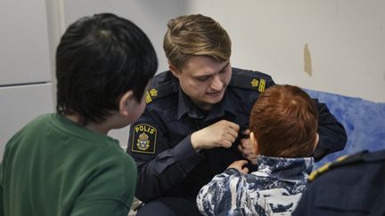 Ett barn är nyfiket på en ficka i en polis uniform. Ett annat barn tittar nyfiket på strax bakom.