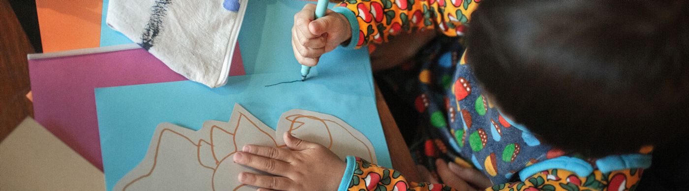 Barn som målar med en penna på ett turkost papper.
