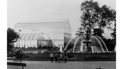 Svartvitt foto av barn som står framför en fontän i Trädgårdsföreningen. Palmhuset syns i bakgrunden.