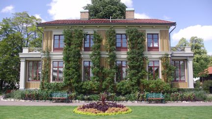 Gul byggnad med röda fönsterkarmar. Det växer klängväxter längst med fasaden, upp till taket.