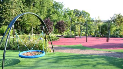Lekplats med blå kompisgunga i förgrunden och flera gungor i bakgrunden.