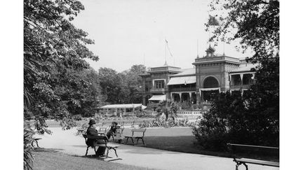 Äldre svartvitt foto på Trädgårdsföreningen, två personer sitter på parkbänkar längst en av stigarna i parken.