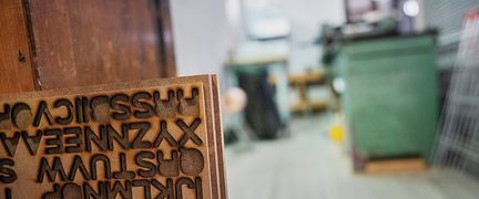 Fotografi, i förgrunden en skylt med bokstäver för tryck (typografi) och i bakgrunden en verkstad med arbetsbänk