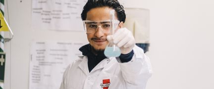 En elev i vit labbrock håller upp ett mätglas med en ljusblå vätska i.