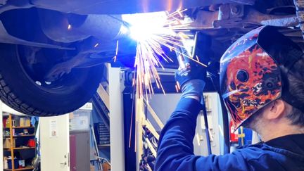 En person svetsar en bil som är upphissad på en lyft.