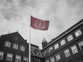 Hvitfeldtskaflaggan i färg mot Norras svartvita fasad