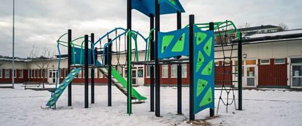 En lekplats framför Tretjärnsskolan med en klätterställning och en rutschkana. I bakgrunden syns en av skolans byggnader.