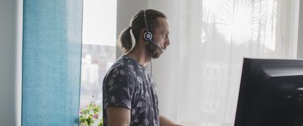En person med headset som står vid ett skrivbord och jobbar vid en dator. 
