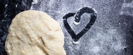 En deg och ett hjärta som är ritat i mjöl på bakbord.