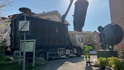Innersäcken från en markbehållare lyfts av sopbil med kran. Bredvid den runda markbehållaren står en sophämtare i gula arbetskläder. 