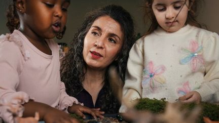 En vuxen är med två barn i förskolemiljö.