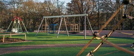 En lekplats utanför Kärralundsskolan med gungor och klätterställningar. En skog syns i bakgrunden.