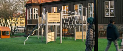 En lekplats utanför Bagaregårdsskolan med en klätterställning och en rutschkana. Några barn kan ses i bakgrunden.