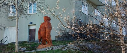 En gorilla i gjutjärn står på en liten bergsknalle framför ett bostadshus. Gorillan blickar upp mot skyn.
