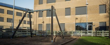 En lekplats framför Skytteskolan med ett par gungor i fokus och ett staket i bakgrunden.