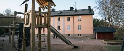 En klätterställning med en rutschkana på en lekplats framför Högenskolan.