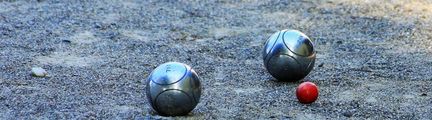 Två bouleklot och en röd liten boll på en grusplan