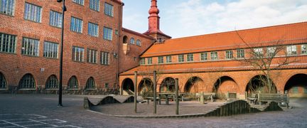 En skolgård med en sandlåda och en skolbyggnad i rött tegel bakom.