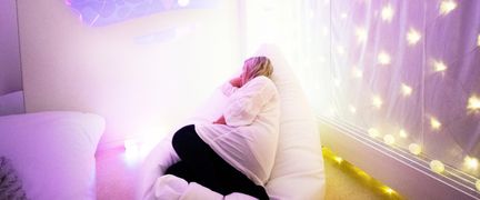 En person ligger i ett sinnesrum med färgat ljus.