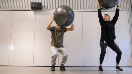 Två personer står och tränar med pilatesbollar. Den ena personens ansikte döljs av bollen.