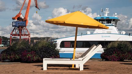 Solstolar och ett gult parasoll vid Stenpiren. I bakgrunden syns en färja och en kran.