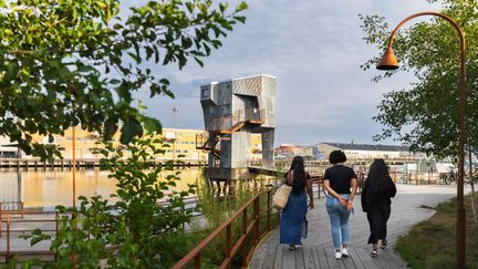 Tre personer går på bryggan ut mot bastun i Jubileumsparken.