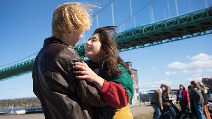 Två ungdomar håller om varandra med Älvsborgsbron i bakgrunden. I bakgrunden syns ett gäng ungdomar.