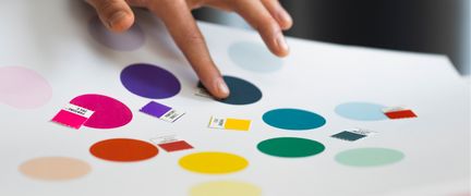 En hand som pekar på ett papper med färgcirklar och färgprover.