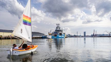 En optimistjolle med ett segeln med regnbågsflaggan på seglar på Göta älv.