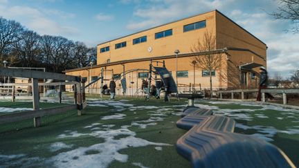 En skolgård med balansgång och lekställning med en skolbyggnad i bakgrunden.