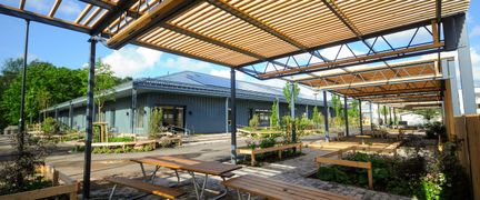 En träpergola som skuggar picknickbord.