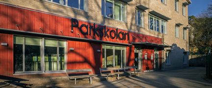 En skolbyggnad med texten Parkskolan på fasaden och bänkar framför.