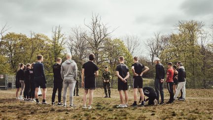 Elever som står i ring och lyssnar på instruktör i militäruniform.