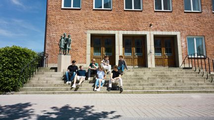 Bild på elever som sitter på trappan utanför Bernadottegymnasiets Entré. Foto av Glory Days