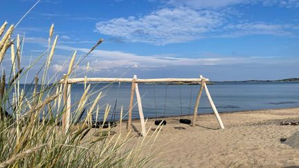 Sandstrand med tre gungor på en träställning.