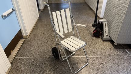 Vit stol med handtag och hjul vid de bakre benen.