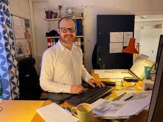 Foto på när Mikael står bakom sitt skrivbord på jobbet.