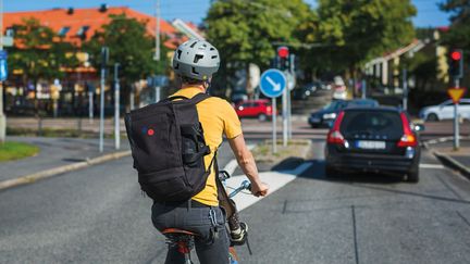 En förälder med gul t-shirt skjutsar sitt barn på sin cykel.