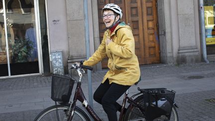 En glad senior med gul jacka cyklar genom stan.