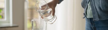 En person häller upp vatten i ett glas från en karaff