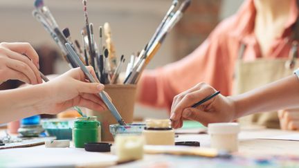 Flera personer sitter vid ett bord och målar. 