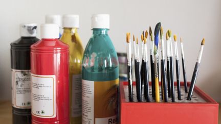 Färgflaskor och ett ställ med penslar.