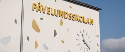En av Påvelundsskolans byggnader med skolans skylt och en klocka i fokus.