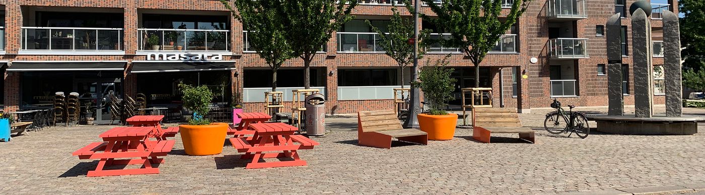 Sittmöbler och orange picknickbord på ett torg.