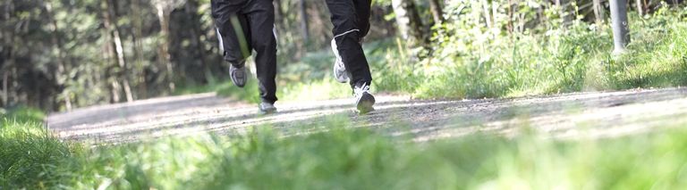 Två joggare ute och springer i skogen på grusväg