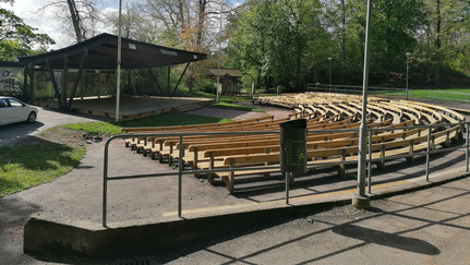 En park med scen och sittbänkar omgiven av natur.