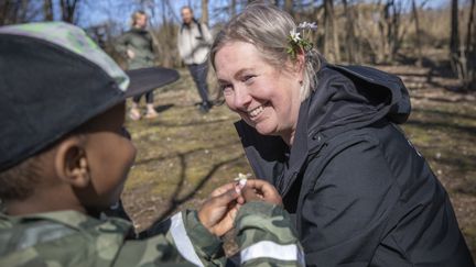 En pojke som håller upp en liten blomma för en kvinna