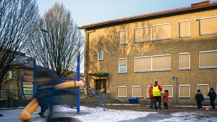 En lekställning och en en grupp barn som leker framför en skolbyggnad.