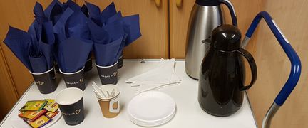 En fikavagn med termosar, muggar, tallrikar och servetter.